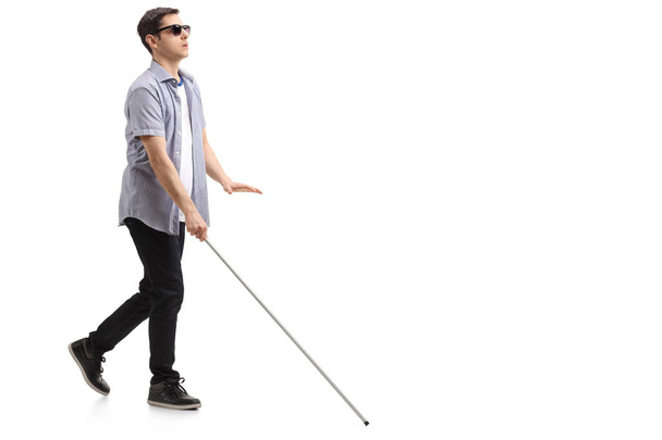 Vollständige Profilaufnahme eines blinden jungen Mannes mit einem Blindenstock, der isoliert auf weißem Hintergrund geht - Foto, Bild
