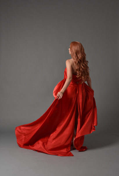 Ganzkörperporträt einer Frau in einem roten Seidenkleid, die auf grauem Studiohintergrund posiert. - Foto, Bild