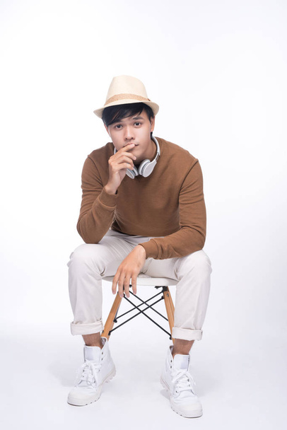 Smart casual asian man seated on chair, posing while looking away in studio background - Photo, Image