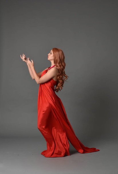 Pełna długość Portret kobiety sobie czerwona, jedwabna sukienka, pozie stojącej na studio szary tło. - Zdjęcie, obraz