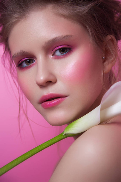 close-up beauty portrait with exotic flower. young caucasian lady isolated on pink background. messy hairstyle. woman with pink make-up. fashion portrait. healthy glowing skin - Foto, imagen