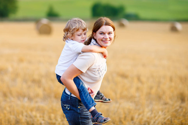 Mother holding kid boy on arms on wheat field in summer - Foto, imagen