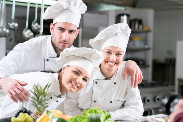 Two glad female and one male young cooks wearing uniform working - Foto, Bild