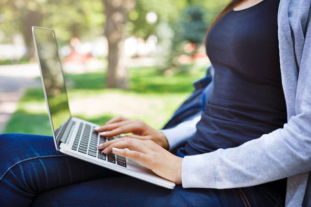 Cropped shot of young brunette woman typing. Working with laptop in the park - 写真・画像