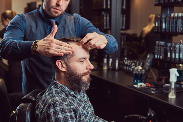 Ein stilvoller Friseurmeister schneidet dem Kunden die Haare. Herrenfrisur in einem Friseursalon. Styling der Haare mit Kamm. - Foto, Bild