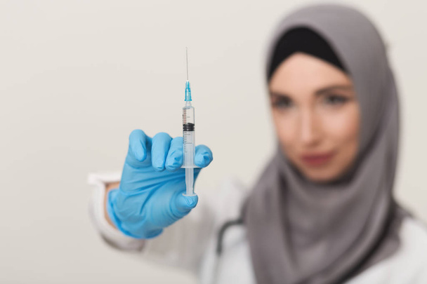 Woman in hijab showing syringe at studio background - Zdjęcie, obraz