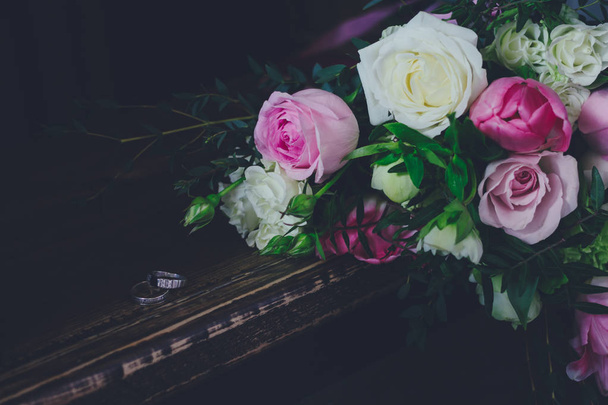 Beautiful toned picture with wedding rings lie on a wooden surface against the background of a bouquet of flowers. - Foto, imagen