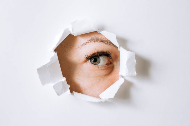 young woman peeks through a hole in a paper white wall - Foto, imagen
