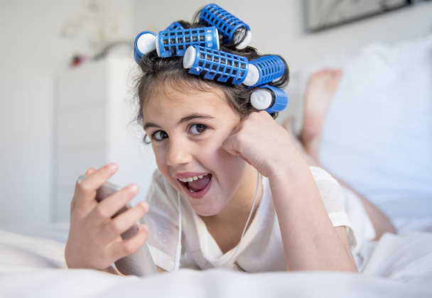 little girl posing with curlers and Smartphone - Фото, зображення