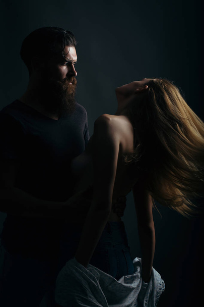 young couple silhouette of handsome bearded man with long beard and pretty sexy woman or girl topless with naked back and red hair in studio on black background - Zdjęcie, obraz