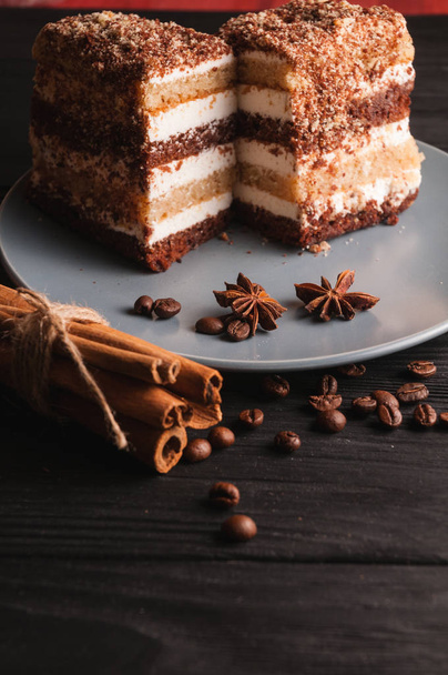 Sweet dessert tiramisu in a cut on a gray plate on a black wooden background with spices: cinnamon sticks and badan, coffee beans. - Foto, imagen