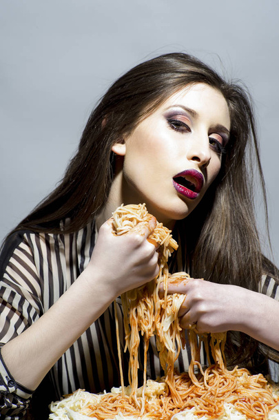 Food, diet and cuisine. Sexy woman eat spaghetti with hands. Woman eat pasta dish with tomato ketchup. Hungry girl have italian food meal. Beauty model with makeup and long brunette hair have dinner. - 写真・画像
