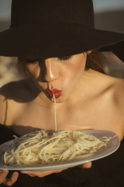 spaghetti in hands of elegant woman in black hat. spaghetti as italian traditional food - Photo, Image