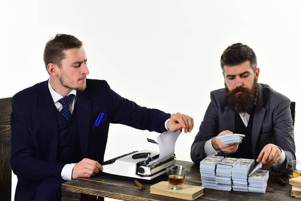 Illegal business concept. Men sitting at table with piles of money and typewriter. Company engaged in illegal business. Businessmen discussing illegal deal while drinking and smoking, white background - Photo, image