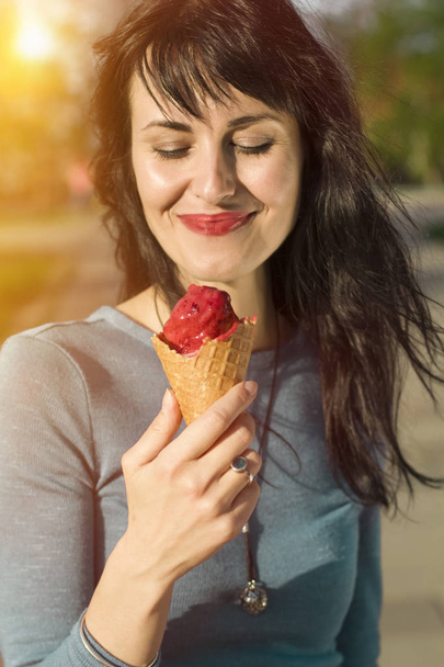 Портрет радісної дівчини з морозивом на фоні сонця. Крупним планом модна, стильна молода жінка, що їсть морозиво в спекотну літню погоду, гарний настрій
.  - Фото, зображення
