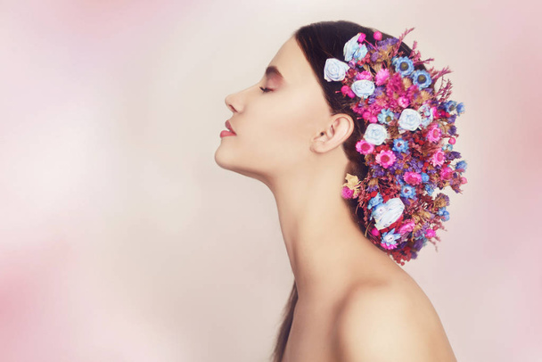 Mooie jonge vrouw met delicate bloemen in hun haar. Schoonheid meisje met bloemen Hairstyle.Model portret met zomerbloemen roze en blauw. Kapsel met bloemen. Fantasie portret in roze. Glimlach. - Foto, afbeelding