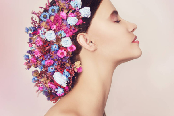 Piękna młoda kobieta z delikatnych kwiatów we włosach. Piękna dziewczyna z kwiatami Hairstyle.Model portret różowy i niebieski kwiaty lato. Fryzura z kwiatami. Portret Fantasy w kolorze różowym. Uśmiech. - Zdjęcie, obraz