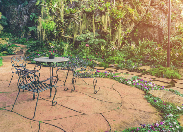 花こう岩のテーブルと金属の椅子と牧歌的な緑豊かな庭園のリラクゼーション エリア。フィルター処理されたヴィンテージトーン イメージ. - 写真・画像