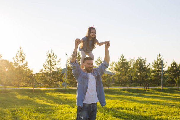 Щасливий батько чоловік тримає свою маленьку дочку на шиї в літньому парку
 - Фото, зображення