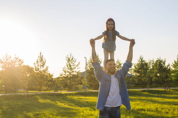 Feliz hombre sosteniendo a su pequeña hija en el cuello en el parque de verano
 - Foto, Imagen
