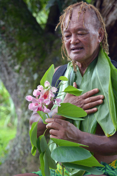 Olde aged Pacific Islander man looks at exotic flower on eco tou - Photo, Image