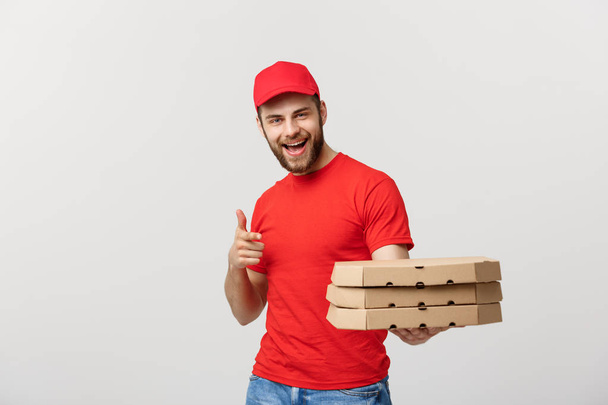 Концепция доставки: Привлекательный кавказский доставщик пиццы, указывающий пальцем. Изолированный на сером фоне
. - Фото, изображение