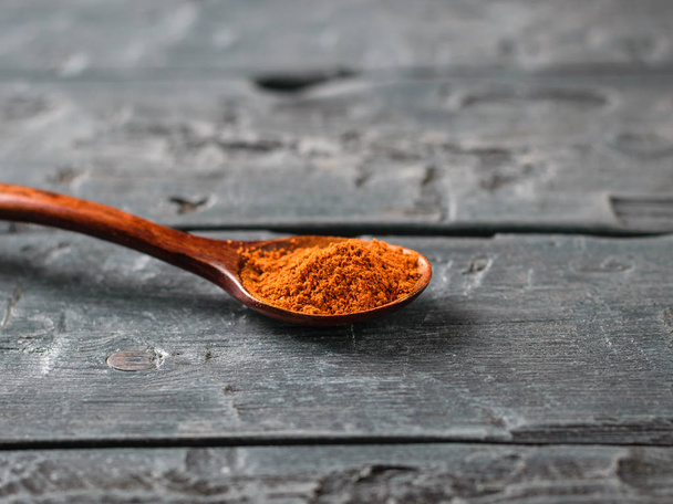 Spoon with crushed red pepper on a dark wooden table. - Foto, Bild