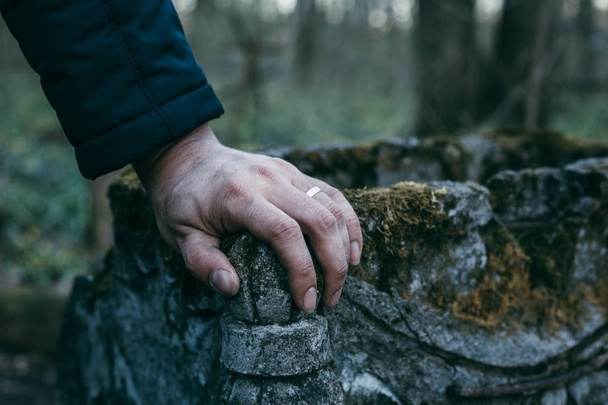Mão de homem sobre lápide antiga coberta de musgo, tristeza e memória eterna para o conceito de pessoas mortas
 - Foto, Imagem