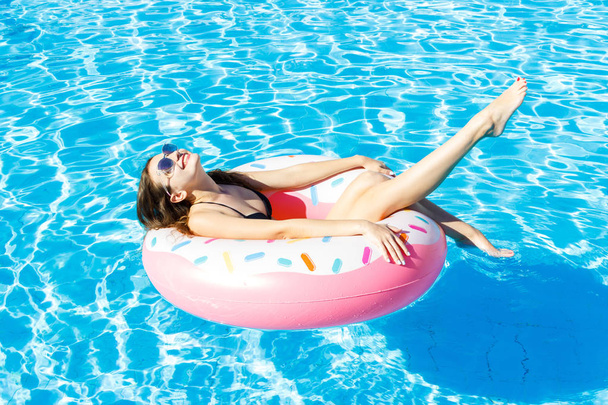 Beautiful young woman with pink circle relaxing in blue swimming pool - Photo, Image
