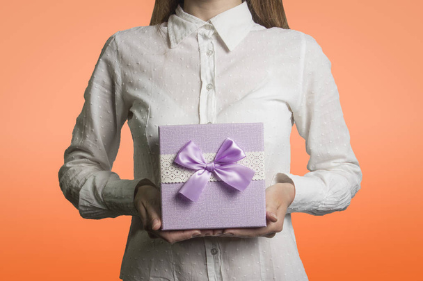 Ein junges Mädchen hält eine Geschenkschachtel auf hellorangefarbenem Hintergrund. die  - Foto, Bild