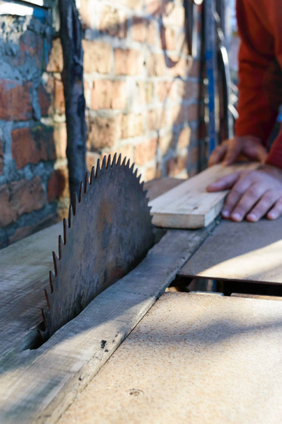 製材所。古い板を製材機です。円形ののこぎり。木工業界。男はボードを押し、それを鋸です。大工の木製まな板の円の鋸を使用して. - 写真・画像