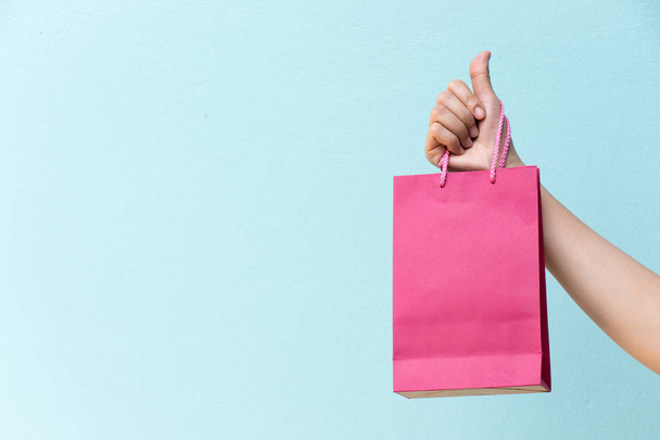 Mano de mujer de negocios sostiene bolsa de compras rosa sobre fondo de hormigón azul
 - Foto, imagen