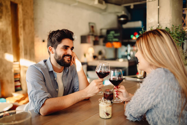 Cheers! Young handsome man is drinking wine with his girlfriend in cafe - Photo, Image