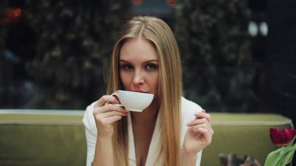 Adorable young woman drinks her coffee sitting in the cafe - Záběry, video