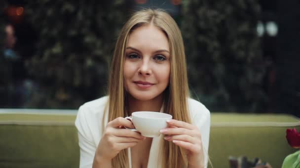 Adorable young woman drinks her coffee sitting in the cafe - Materiaali, video