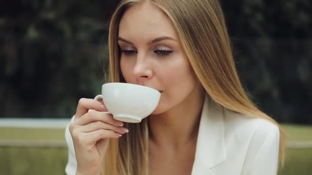 Suloinen nuori nainen juo kahviaan kahvilassa.
 - Materiaali, video