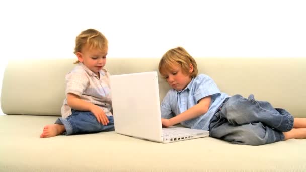 白いソファの上のラップトップ コンピューターで遊ぶ 2 つの小さな男の子 - 映像、動画