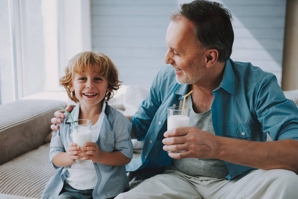 Happy little grandson drinks milk with straw in glass with grandfather. - Foto, afbeelding
