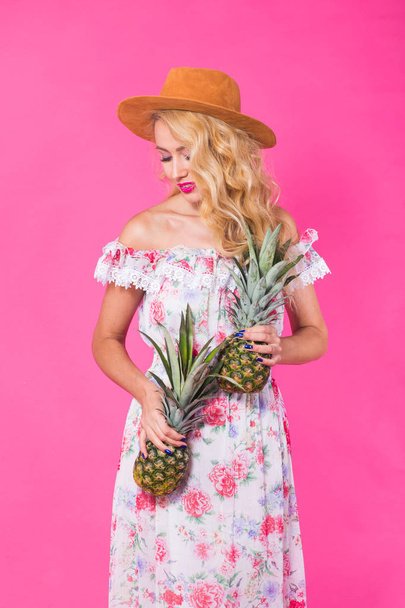 Happy young woman holding a pineapple on a pink background. Summer, diet and holidays concept - Foto, Imagen