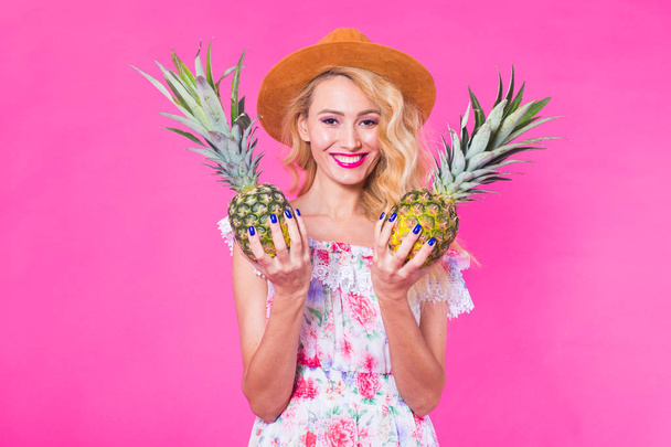 Boldog fiatal nő egy ananász gazdaság egy rózsaszín háttér. Nyáron, a táplálkozás és az ünnepek koncepció - Fotó, kép