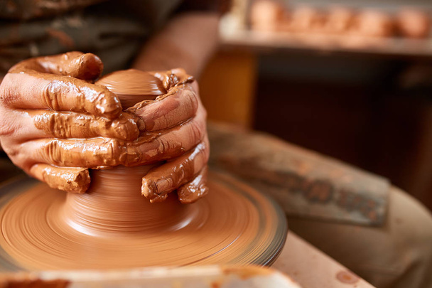 Close-up hands of a male potter in apron making a vase from clay, selective focus - 写真・画像