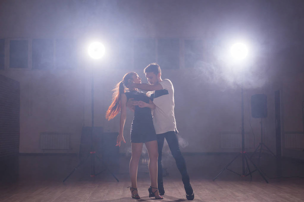 Искусные танцоры выступают в темной комнате под концертным светом и дымом. Чувственная пара, исполняющая художественный и эмоциональный современный танец
 - Фото, изображение