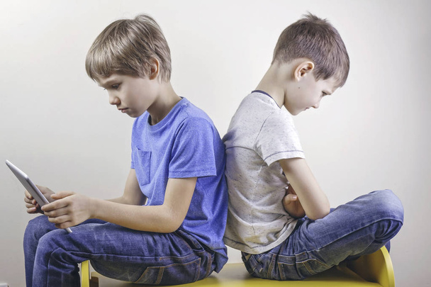 Vício em computadores. Um menino usando tablet e outro garoto sentado com raiva depois de muito tempo jogando jogo
 - Foto, Imagem