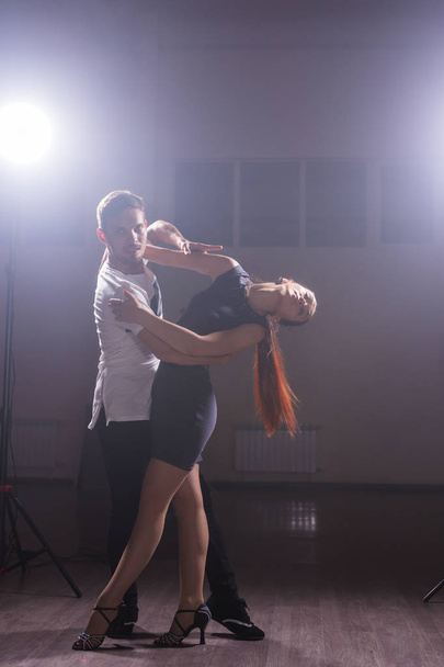 Skillful dancers performing in the dark room under the concert light and smoke. Sensual couple performing an artistic and emotional contemporary dance - Photo, Image
