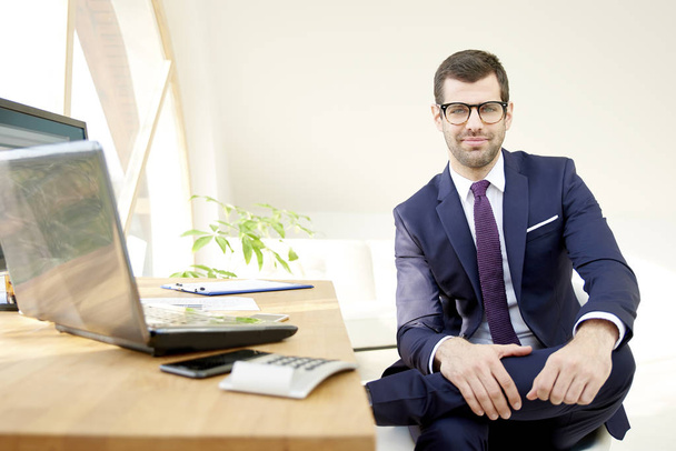 Successful investment advisor businessman wearing suit and looking at camera while sitting at office desk. - Foto, Bild