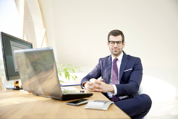 Successful investment advisor businessman wearing suit and looking at camera while sitting at office desk. - Fotoğraf, Görsel