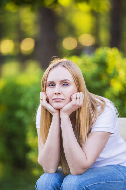 Emotions of the girl, fatigue, boredom, depression, sadness. Attractive bored young blond Caucasian woman holding her head with hands, sits outside in the park - Fotó, kép