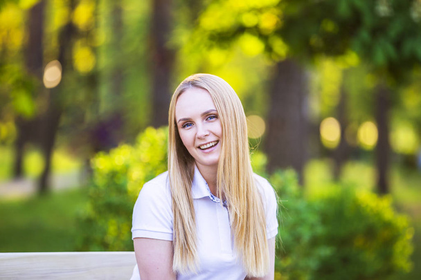 Young, happy, thin young blond woman with long beautiful hair, smiling, in the summer park under the rays of the sun - Фото, зображення