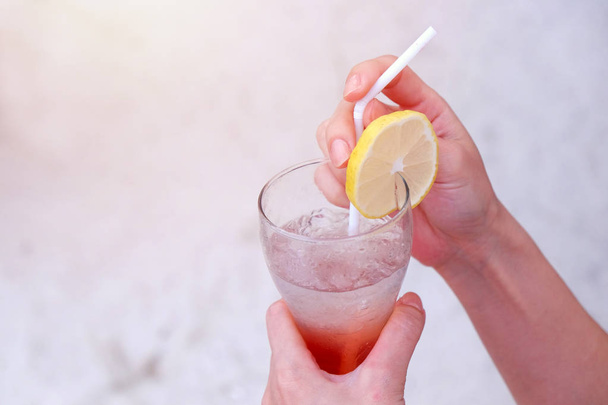 Manos de mujer sosteniendo vaso de bebida helada de verano con limón en rodajas en la playa de arena
  - Foto, Imagen