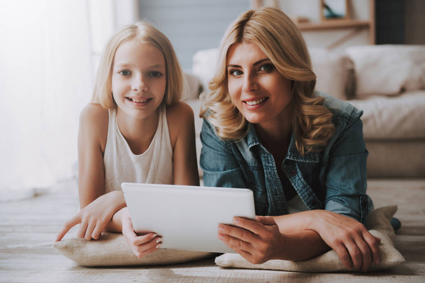 Mature blond woman with cute daughter watching tablet while lying on floor. - Foto, Bild
